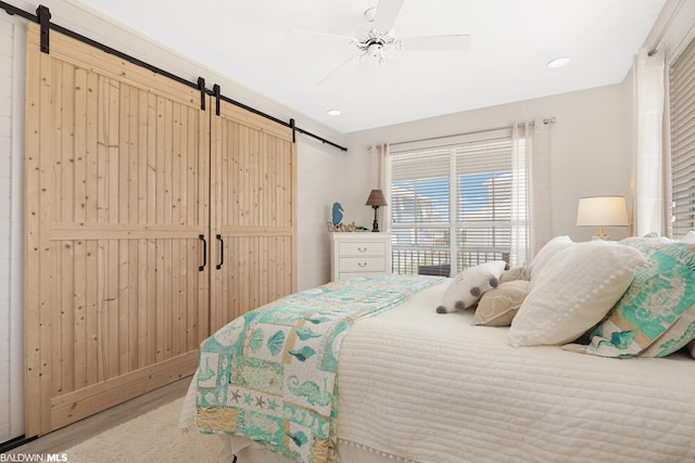 bedroom with a barn door, ceiling fan, and light wood-type flooring