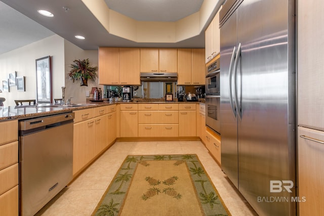 kitchen featuring light brown cabinets, stainless steel appliances, dark stone counters, and light tile floors