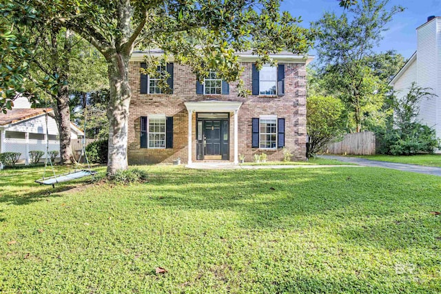 colonial house featuring a front yard, brick siding, and fence