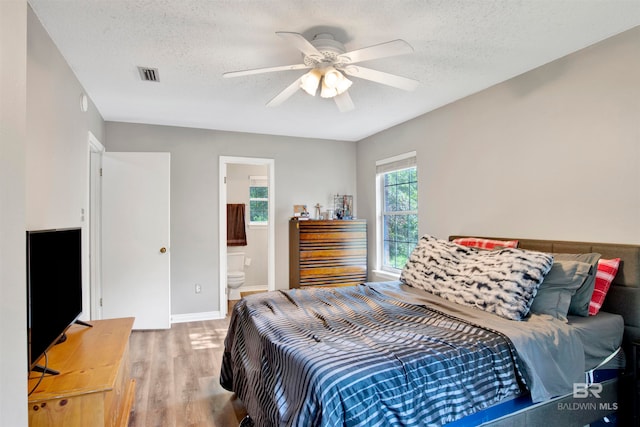 bedroom with ceiling fan, connected bathroom, light hardwood / wood-style flooring, and a textured ceiling