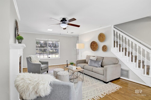 living room with light hardwood / wood-style floors, crown molding, ceiling fan, and a fireplace