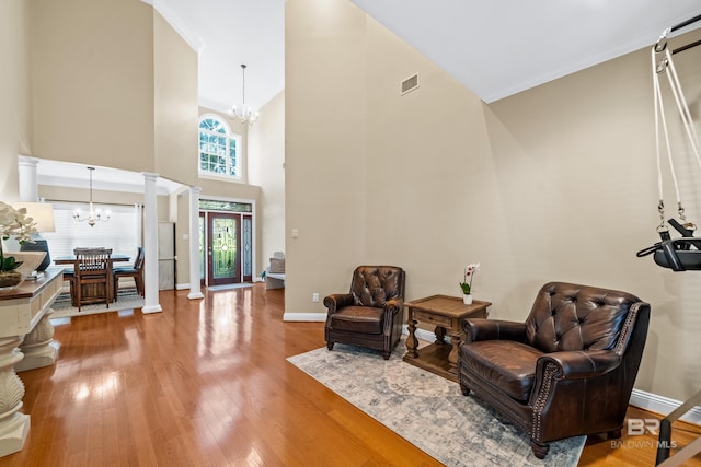 sitting room featuring wood-type flooring, decorative columns, ornamental molding, and an inviting chandelier