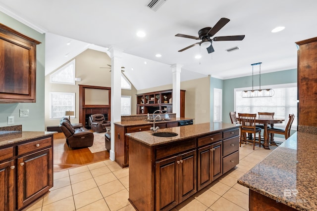 kitchen with dark stone counters, a center island, vaulted ceiling, light tile patterned floors, and ornate columns