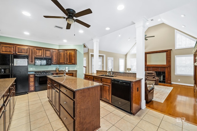 kitchen featuring light tile patterned floors, a center island with sink, ornate columns, and black appliances