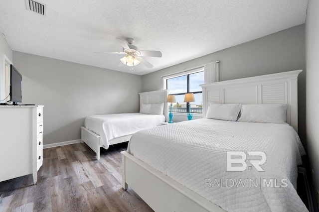 bedroom with visible vents, a textured ceiling, wood finished floors, baseboards, and ceiling fan