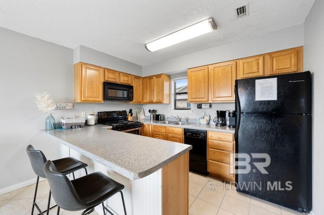 kitchen with visible vents, a peninsula, a kitchen breakfast bar, black appliances, and a sink