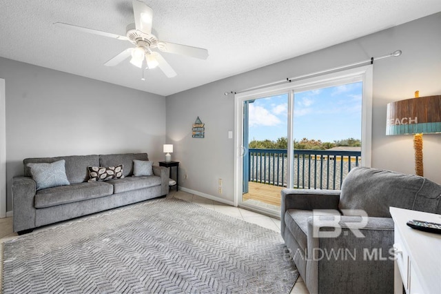 living area featuring ceiling fan, light tile patterned flooring, baseboards, and a textured ceiling