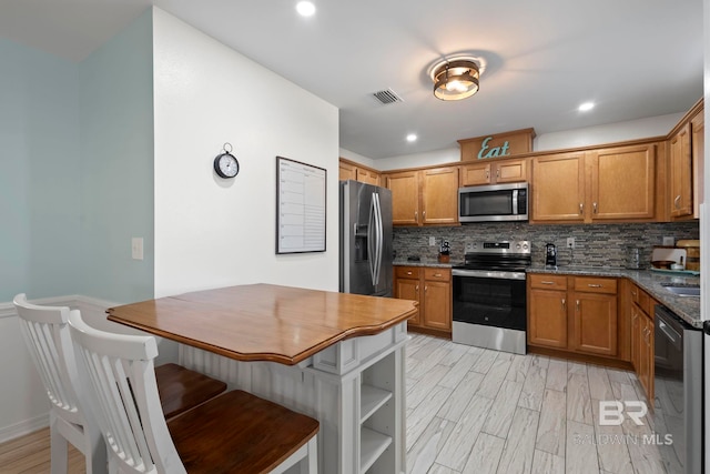 kitchen featuring visible vents, stainless steel appliances, brown cabinetry, light wood finished floors, and decorative backsplash