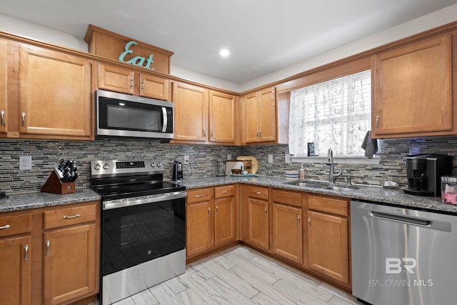 kitchen with brown cabinets, a sink, tasteful backsplash, dark stone counters, and appliances with stainless steel finishes