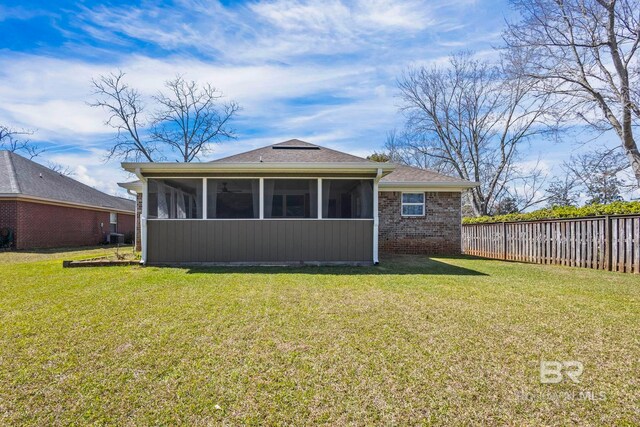 rear view of house with fence, a lawn, brick siding, and a sunroom