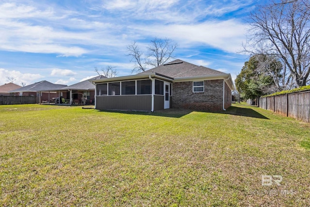 back of house featuring a yard, fence, brick siding, and a sunroom