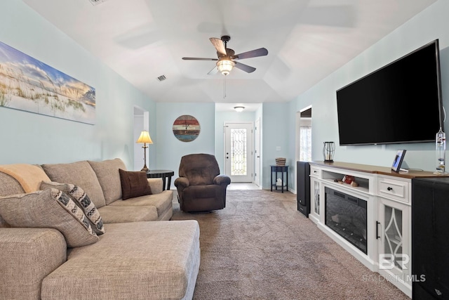 carpeted living area with visible vents, a ceiling fan, a glass covered fireplace, baseboards, and lofted ceiling