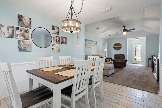 dining space featuring ceiling fan with notable chandelier, lofted ceiling, light wood-style floors, and visible vents