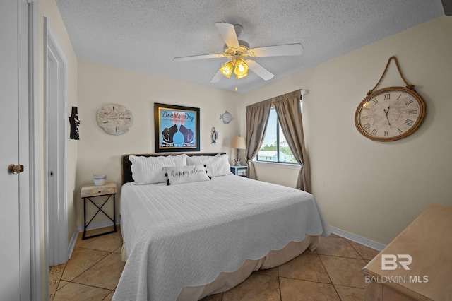 bedroom featuring light tile patterned floors, ceiling fan, baseboards, and a textured ceiling