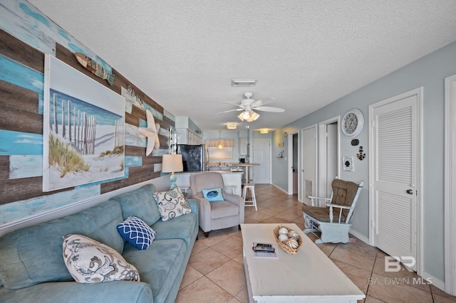 living room featuring ceiling fan, light tile patterned floors, a textured ceiling, and baseboards