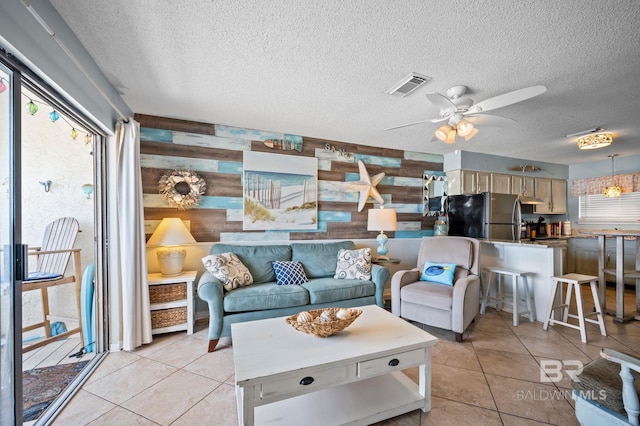 living area featuring a textured ceiling, light tile patterned floors, a ceiling fan, and wood walls