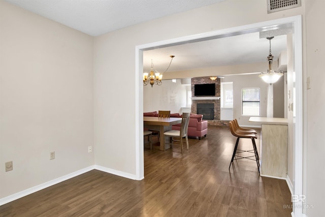 dining area with a brick fireplace, dark hardwood / wood-style floors, a textured ceiling, and a chandelier