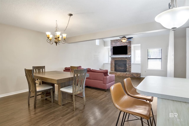 dining room featuring dark hardwood / wood-style flooring, ceiling fan with notable chandelier, a brick fireplace, and a textured ceiling