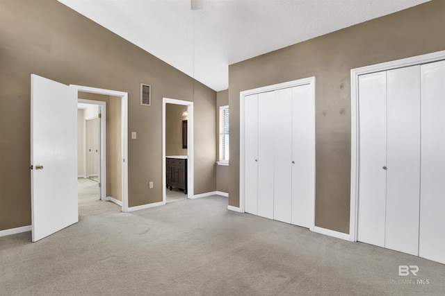 unfurnished bedroom with vaulted ceiling, light colored carpet, ceiling fan, multiple closets, and ensuite bath