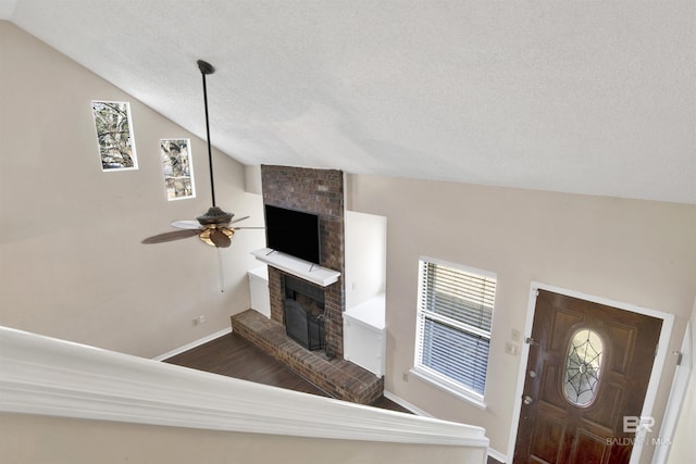 interior space with vaulted ceiling, a fireplace, dark hardwood / wood-style flooring, ceiling fan, and a textured ceiling