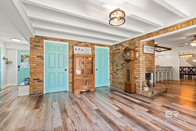 foyer featuring beam ceiling, wood finished floors, and brick wall