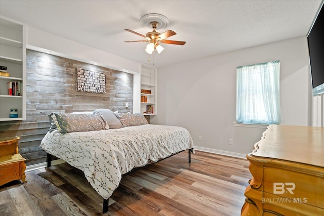 bedroom with baseboards, a textured ceiling, wood finished floors, and a ceiling fan