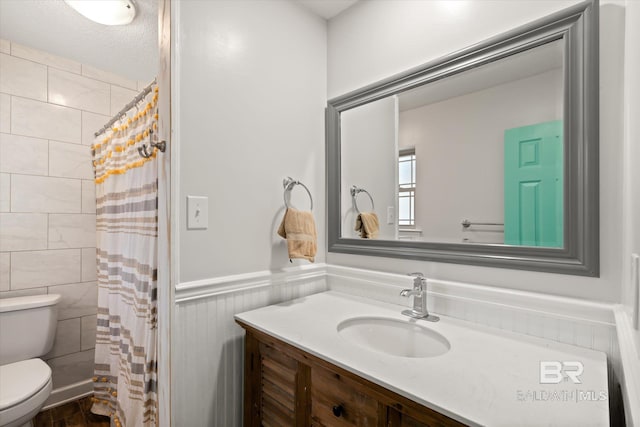 full bathroom with a shower with shower curtain, vanity, toilet, and wainscoting