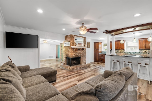 living area with light wood-type flooring, visible vents, a brick fireplace, and crown molding