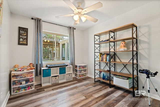 playroom with a ceiling fan, wood finished floors, and baseboards