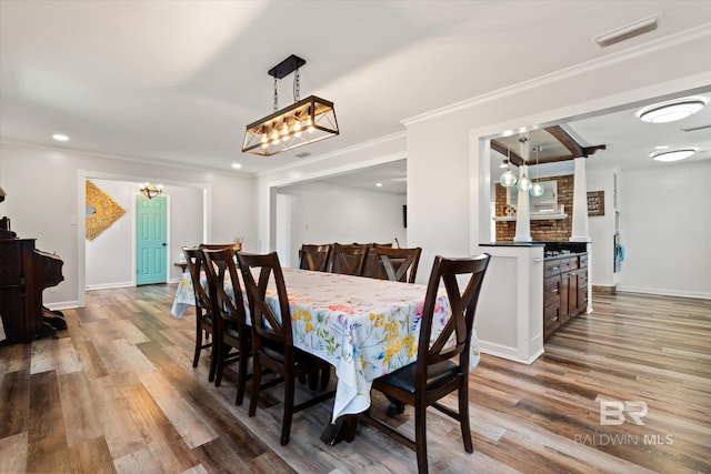 dining area with baseboards, wood finished floors, visible vents, and ornamental molding