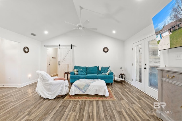 living room with visible vents, lofted ceiling, a barn door, french doors, and wood finished floors