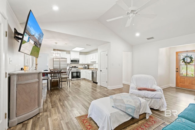 living room featuring visible vents, baseboards, light wood-style floors, and vaulted ceiling