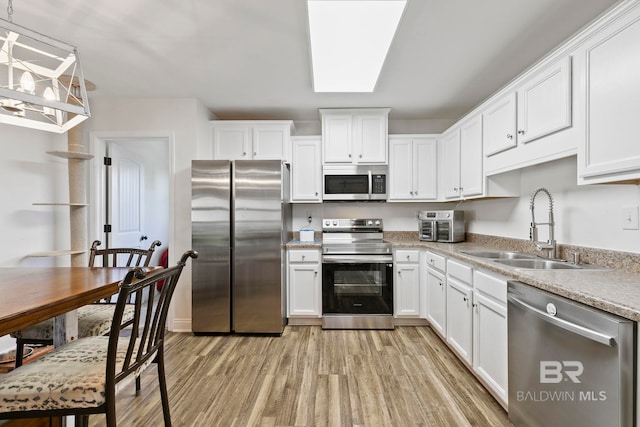 kitchen with a sink, stainless steel appliances, light wood-style floors, and white cabinets