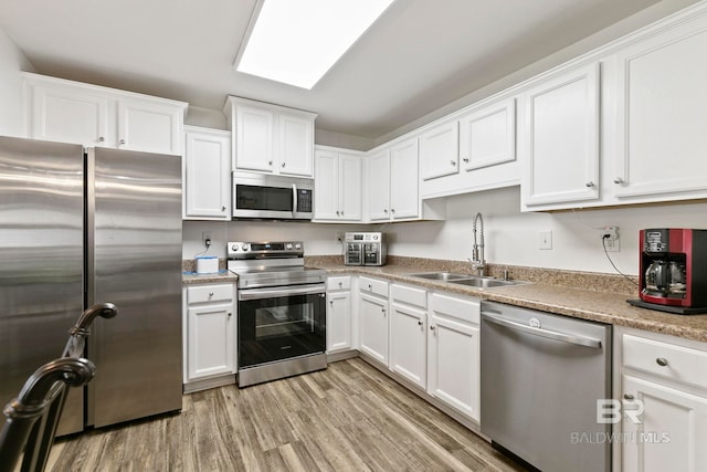 kitchen featuring light wood-style flooring, a sink, stainless steel appliances, white cabinets, and light countertops