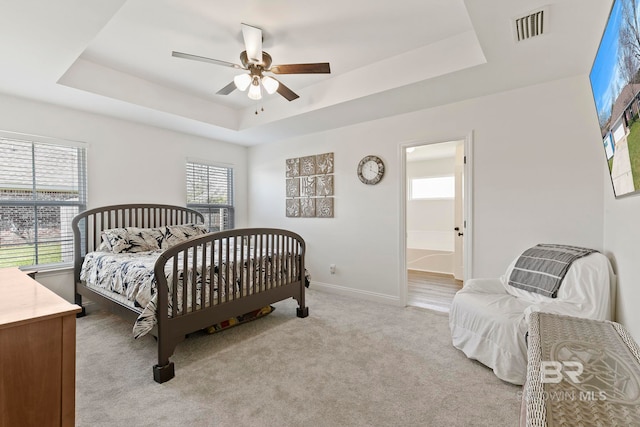 bedroom featuring a raised ceiling, baseboards, visible vents, and light carpet