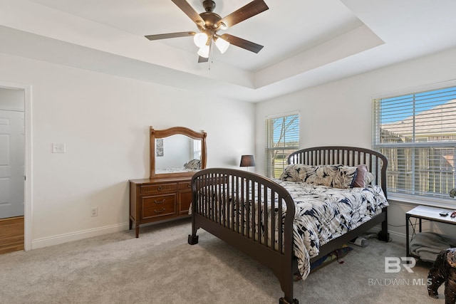 carpeted bedroom featuring a ceiling fan, a raised ceiling, and baseboards