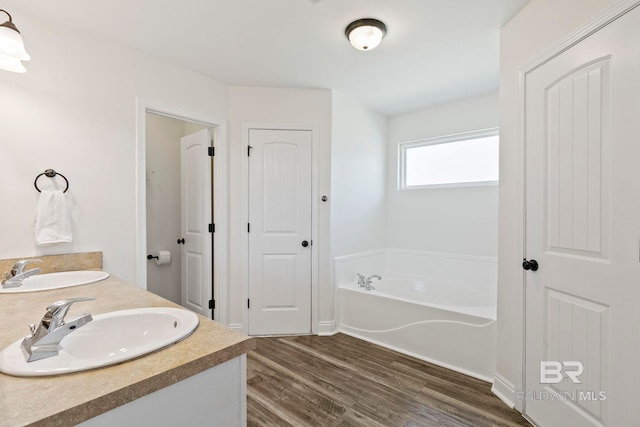 full bath featuring double vanity, wood finished floors, a garden tub, and a sink