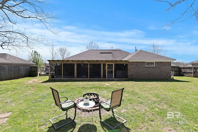 back of property featuring a fenced backyard, an outdoor fire pit, a yard, a sunroom, and brick siding