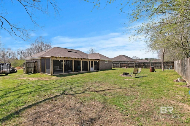 view of yard with a fire pit, a fenced backyard, and a sunroom