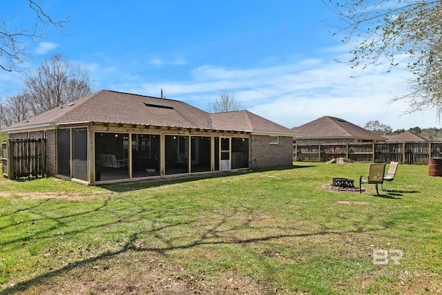 rear view of house featuring a fenced backyard, a fire pit, brick siding, and a sunroom