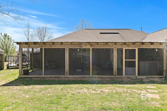 rear view of house featuring a lawn, a sunroom, and roof with shingles