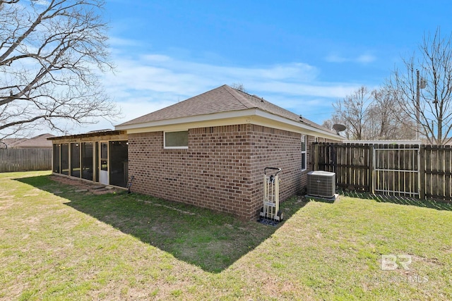 rear view of property featuring brick siding, central AC unit, a yard, and a sunroom