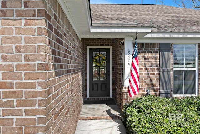 doorway to property with brick siding and roof with shingles