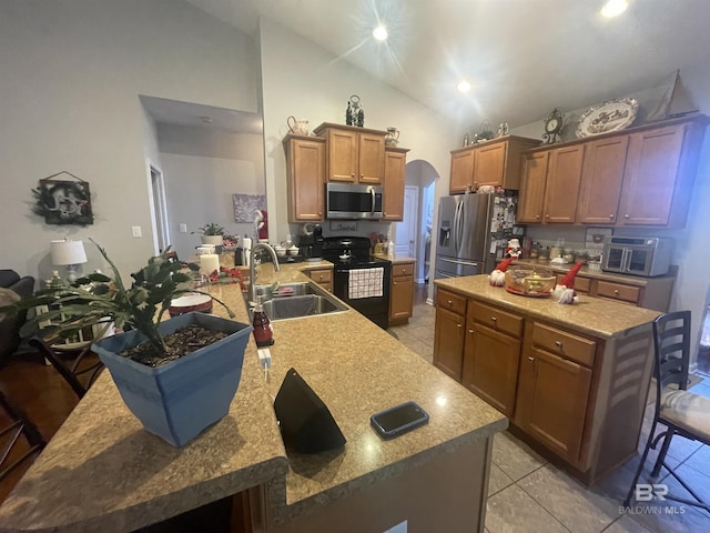 kitchen with kitchen peninsula, appliances with stainless steel finishes, a kitchen breakfast bar, sink, and light tile patterned floors