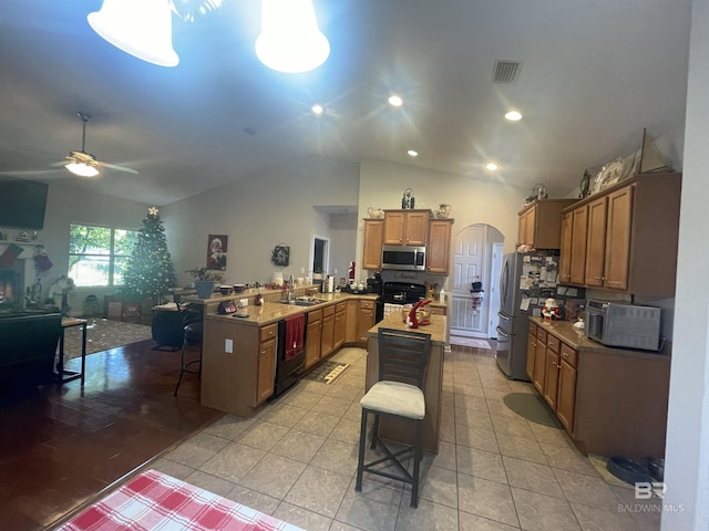 kitchen featuring light tile patterned floors, vaulted ceiling, a breakfast bar area, and black appliances