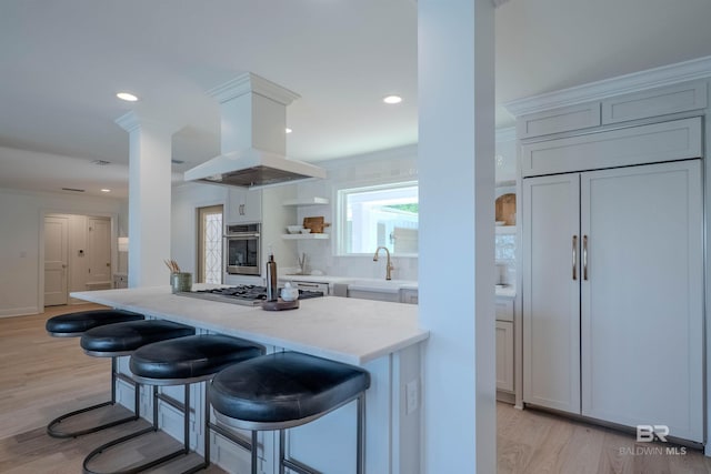 kitchen with a kitchen bar, appliances with stainless steel finishes, light wood-type flooring, extractor fan, and sink