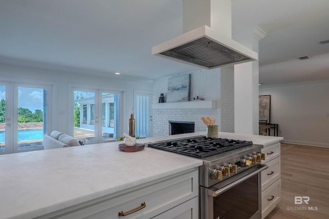 kitchen featuring high end range, a fireplace, light hardwood / wood-style flooring, white cabinets, and range hood