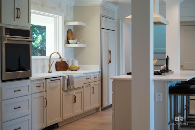 kitchen featuring ornamental molding, stainless steel oven, extractor fan, sink, and light hardwood / wood-style flooring