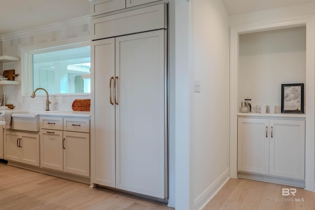 kitchen with light hardwood / wood-style floors, paneled refrigerator, white cabinetry, and sink