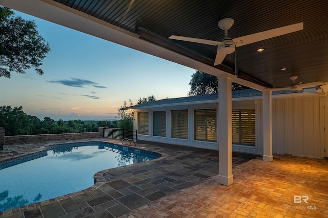 pool at dusk featuring ceiling fan and a patio area